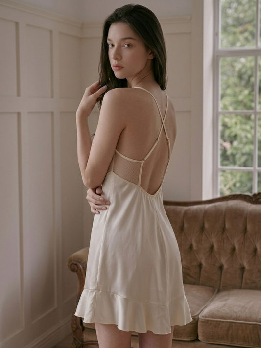 Woman wearing a beige dress with thin straps in a room with a brown sofa and window.