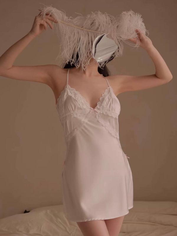 Woman in a white satin nightgown holding feathers against a neutral background