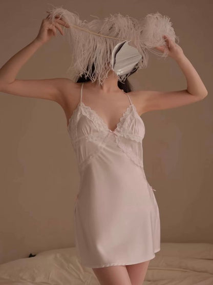Woman in a white satin nightgown holding feathers against a neutral background