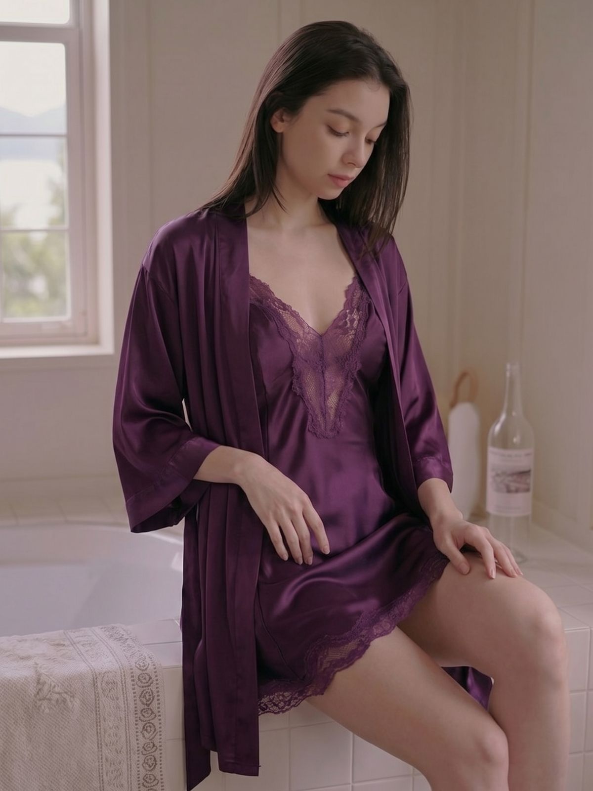 Woman in a purple satin robe sitting on a bathtub edge in a bathroom.