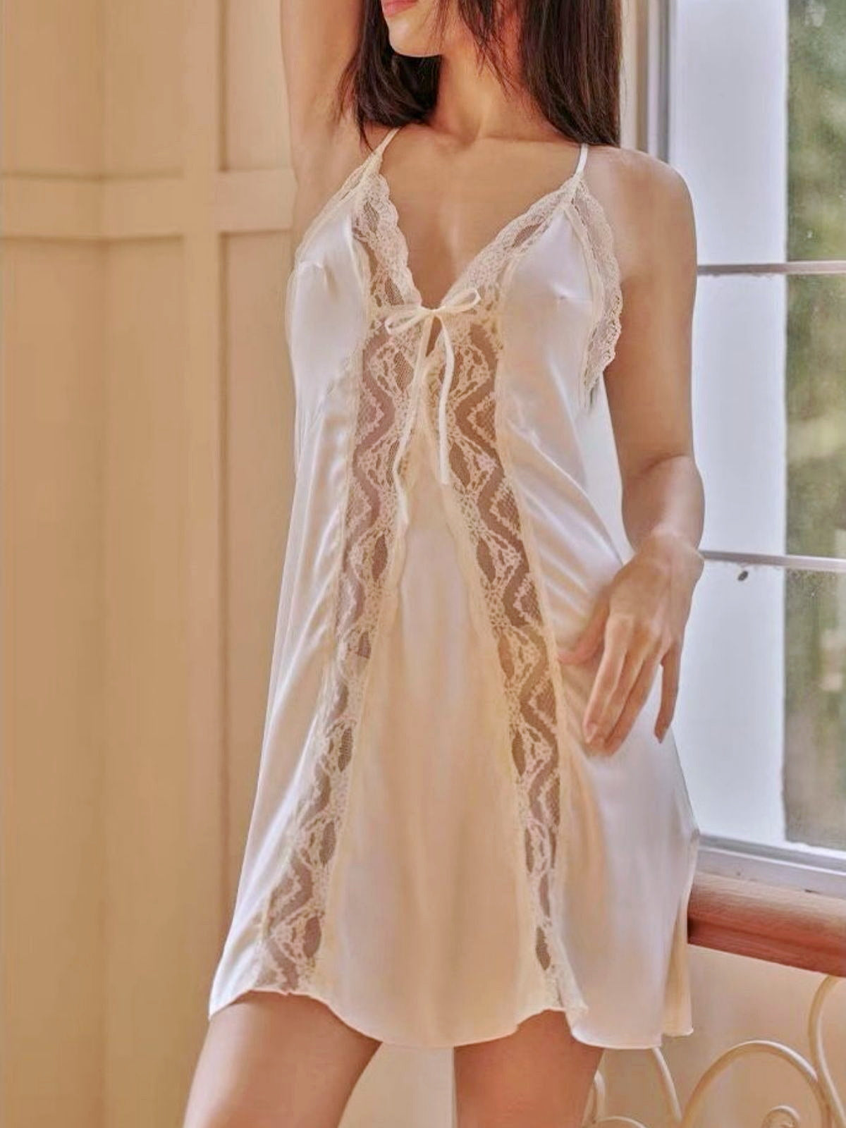 Woman wearing a white lace nightgown in a softly lit room.