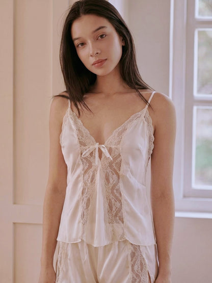 Woman wearing a white lace camisole in a softly lit room.