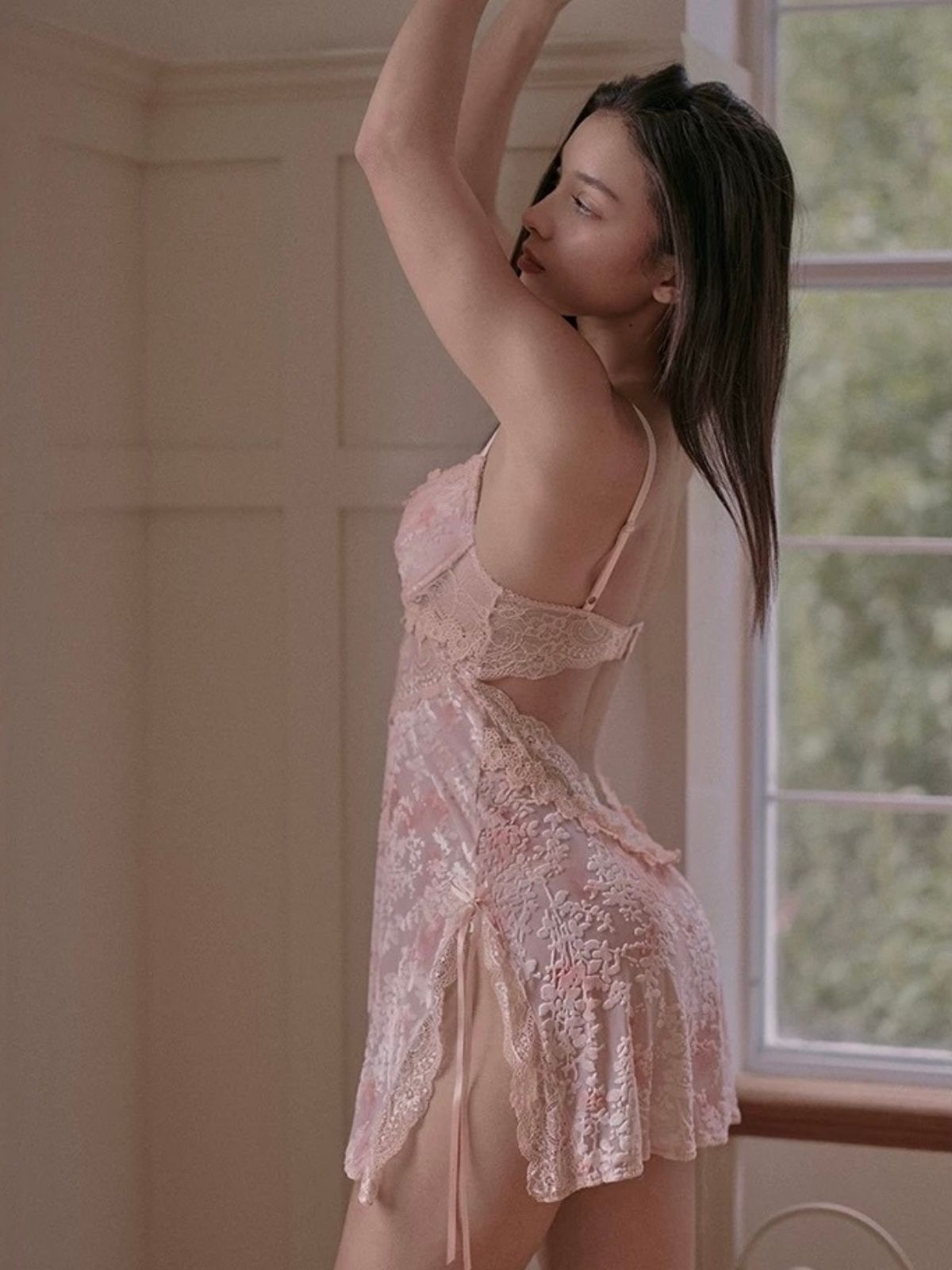 Woman wearing a pink lace nightgown  in velvet material in a softly lit room.