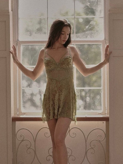 Woman in a green lace velvet material nightgown standing in front of a window with a blurred outdoor view.