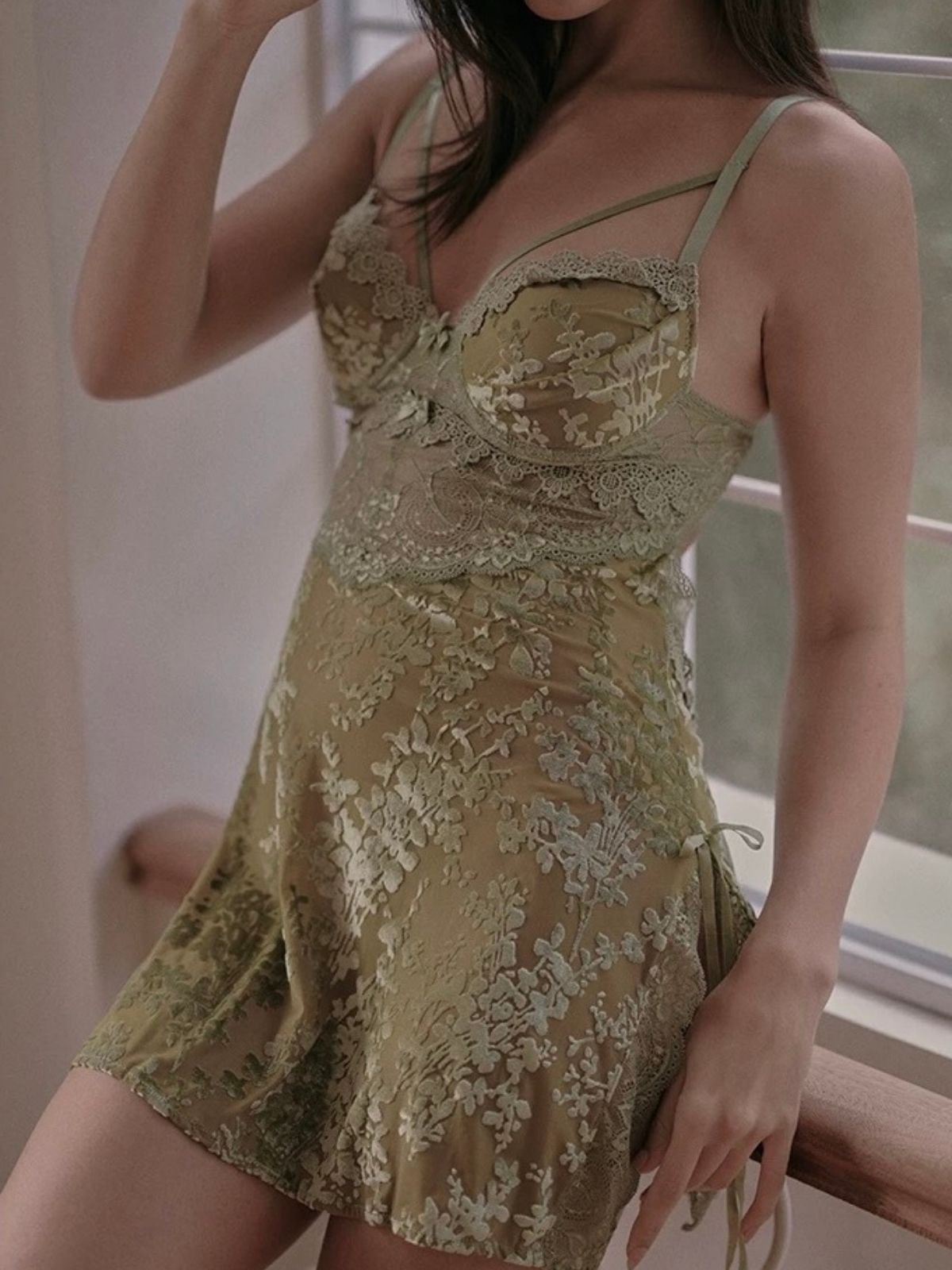 Woman wearing a green lace dress sitting indoors.