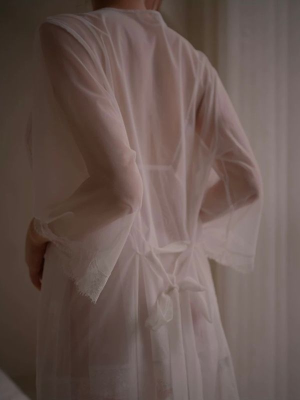 Person wearing a light pink robe with lace trim in a softly lit room.