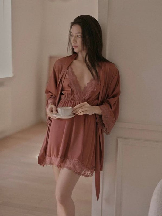 Woman in a brown robe and chemise holding a cup in a softly lit room.