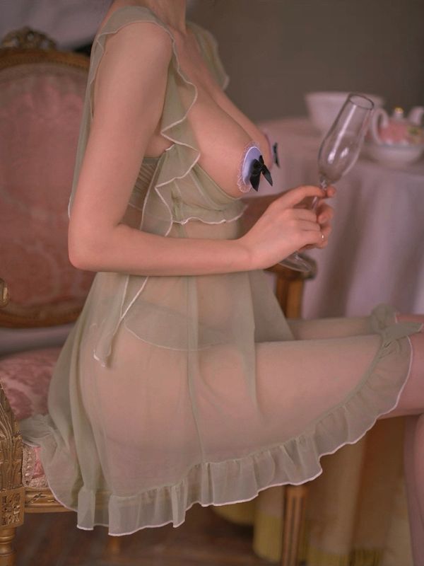Person wearing a sheer green open bust lingerie holding a glass in an indoor setting.