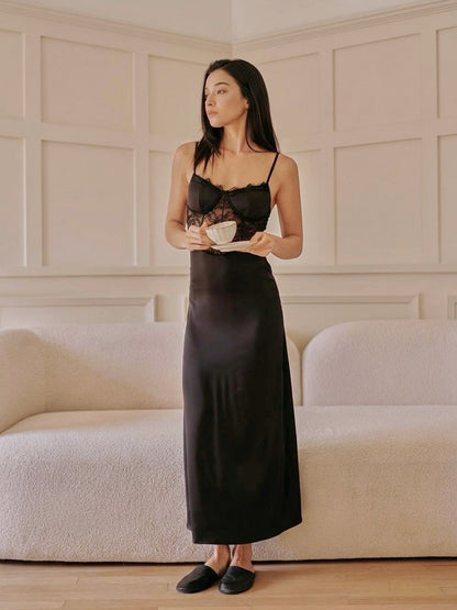 Woman in a long black satin slip dress standing in a room with a neutral color scheme.