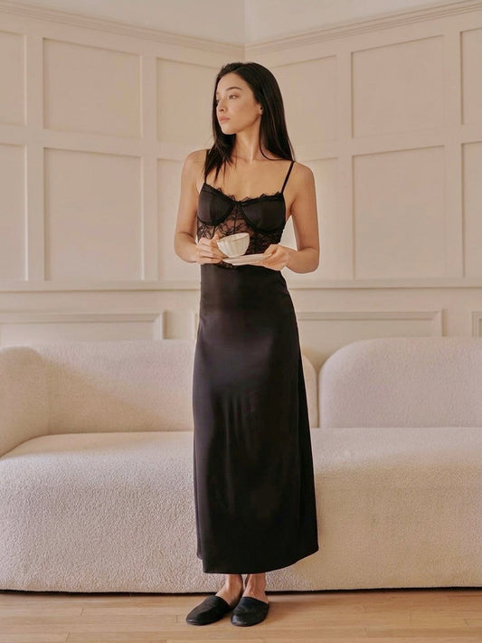 Woman in a long black satin slip dress standing in a room with a neutral color scheme.