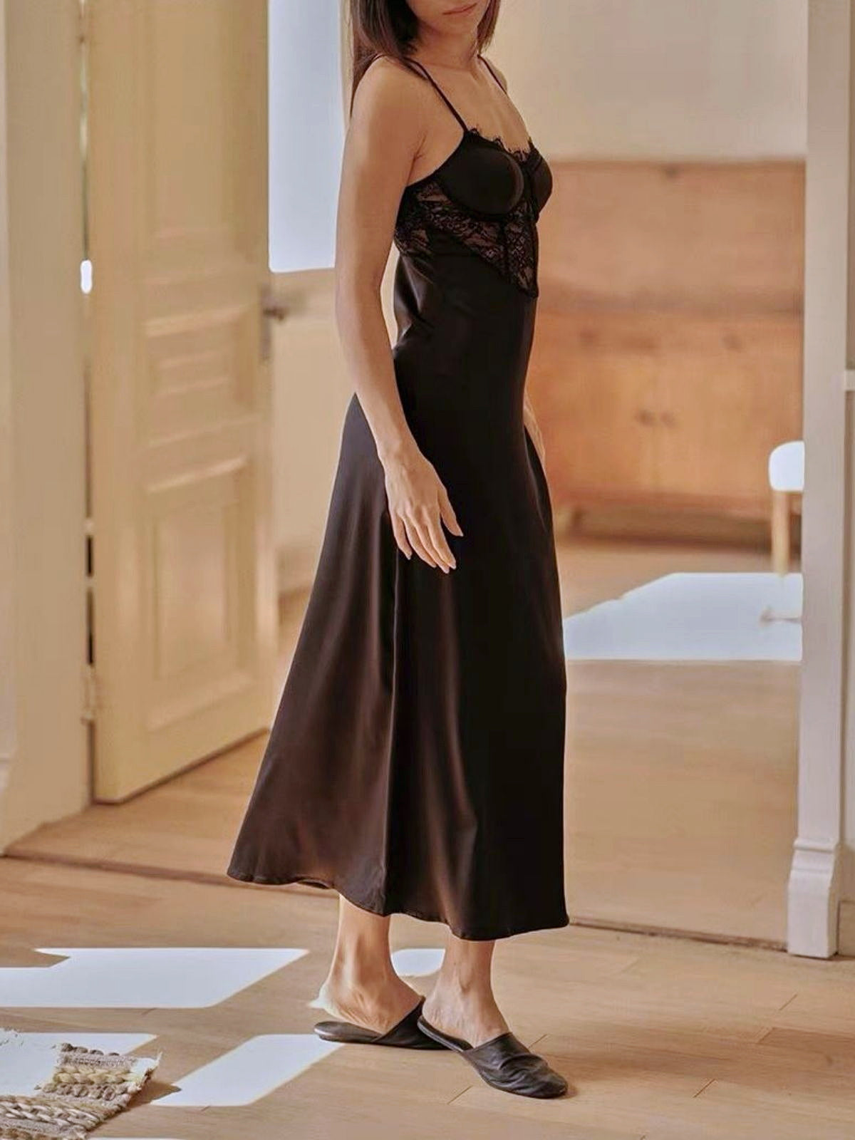 Woman wearing a black slip dress in a room with wooden flooring.