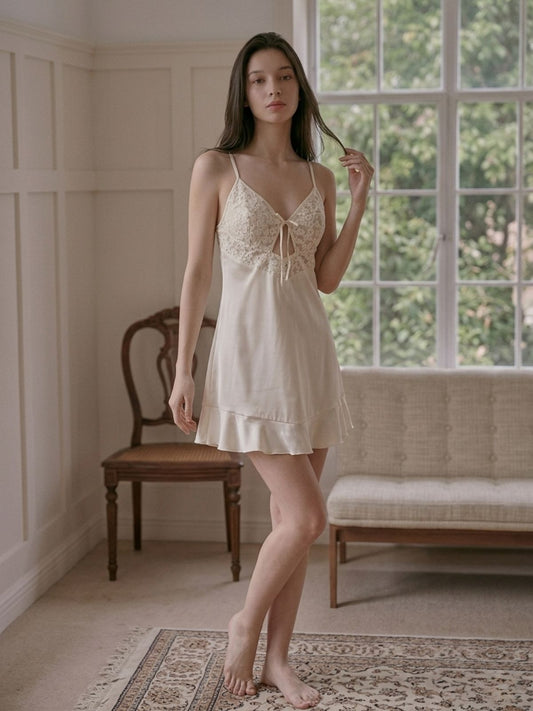 Woman wearing a beige lace nightgown in a softly lit room with large windows.